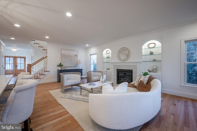 living room with a wealth of natural light, french doors, ornamental molding, and light wood-type flooring