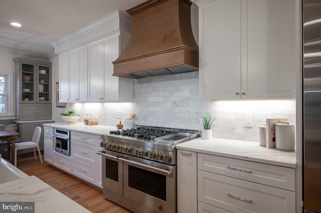 kitchen with custom exhaust hood, white cabinetry, high quality appliances, and light stone countertops