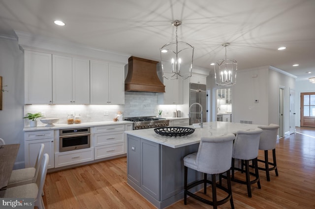 kitchen featuring white cabinetry, appliances with stainless steel finishes, a kitchen island with sink, and custom exhaust hood