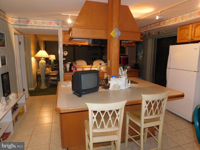 kitchen featuring a breakfast bar, white refrigerator, rail lighting, vaulted ceiling, and light tile patterned floors