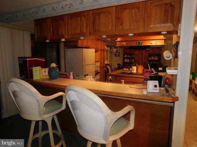 kitchen with white fridge, a kitchen bar, and light tile patterned floors