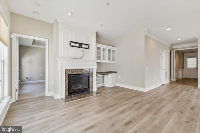 unfurnished living room with light wood-type flooring, a high end fireplace, and ornamental molding