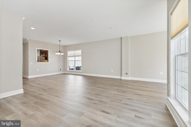 unfurnished room with light wood-type flooring and an inviting chandelier