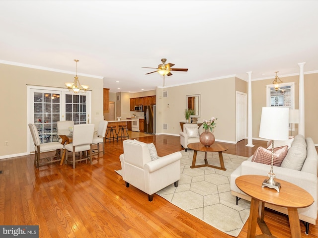 living room with decorative columns, ceiling fan with notable chandelier, light wood-type flooring, and ornamental molding