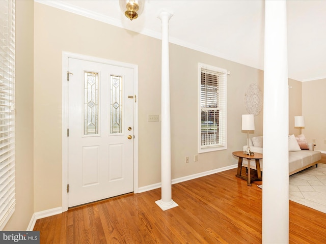 foyer with light hardwood / wood-style floors, crown molding, and decorative columns