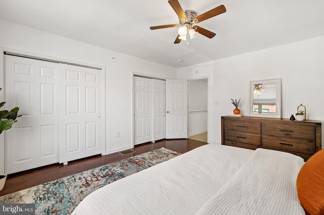 bedroom featuring dark hardwood / wood-style flooring, ceiling fan, and two closets