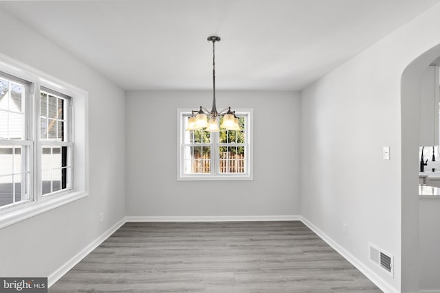 unfurnished dining area with a chandelier, a wealth of natural light, and light hardwood / wood-style flooring