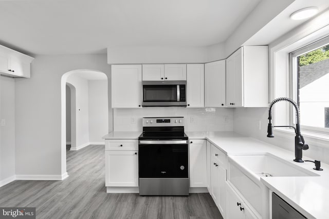 kitchen featuring stainless steel appliances, white cabinets, decorative backsplash, sink, and light wood-type flooring