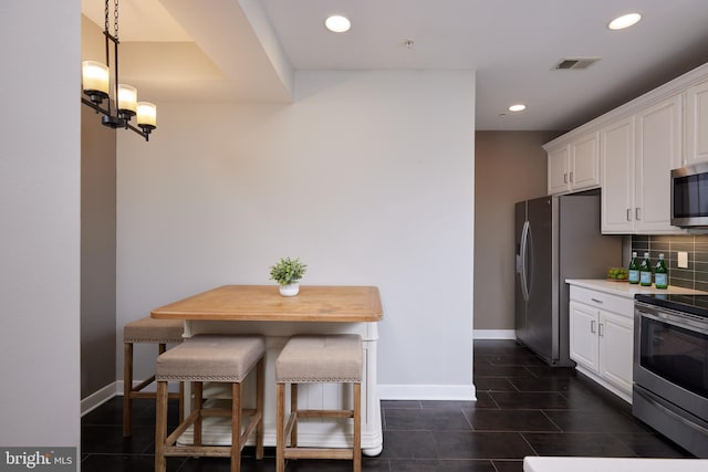 kitchen with stainless steel appliances, hanging light fixtures, backsplash, a breakfast bar, and white cabinetry