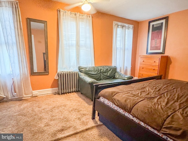 carpeted bedroom with ceiling fan, multiple windows, and radiator heating unit