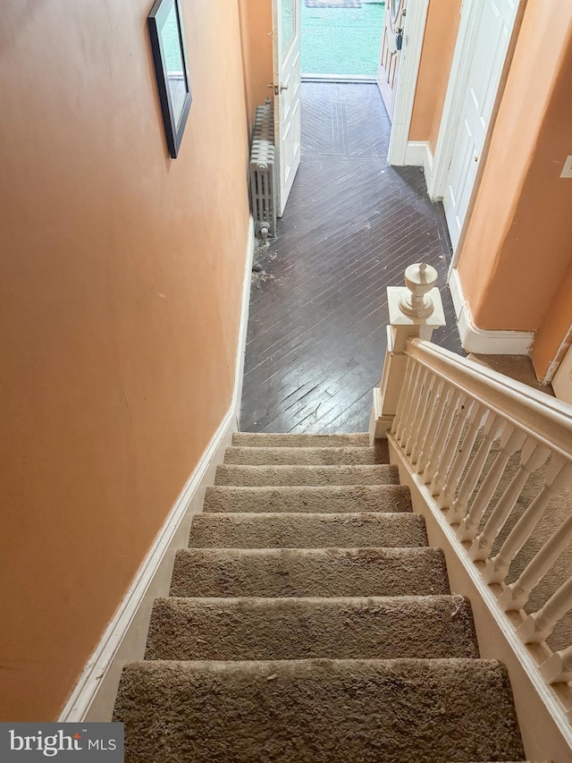 stairway with hardwood / wood-style floors, plenty of natural light, and radiator heating unit