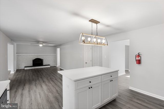 kitchen with a ceiling fan, baseboards, a brick fireplace, dark wood finished floors, and a kitchen island