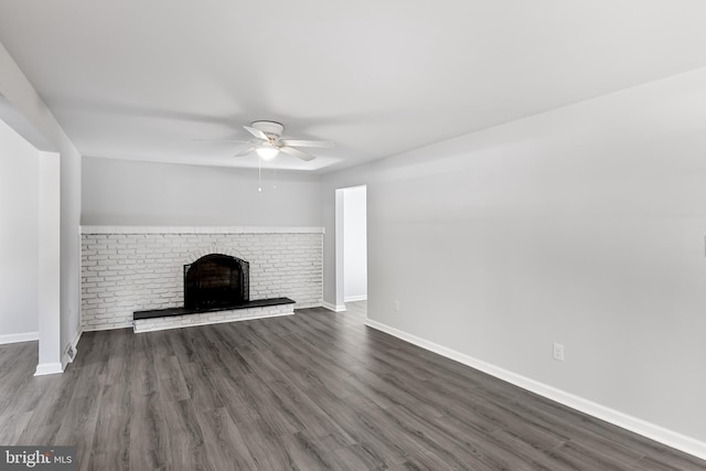 unfurnished living room with ceiling fan, dark wood finished floors, a brick fireplace, and baseboards