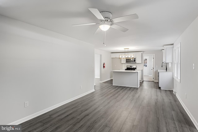unfurnished living room with a chandelier, dark wood-style flooring, a ceiling fan, a sink, and baseboards