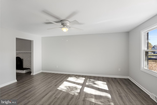 unfurnished living room with dark wood-style flooring, ceiling fan, baseboards, and a brick fireplace