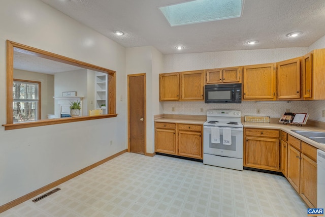 kitchen featuring sink, vaulted ceiling with skylight, white appliances, and a textured ceiling