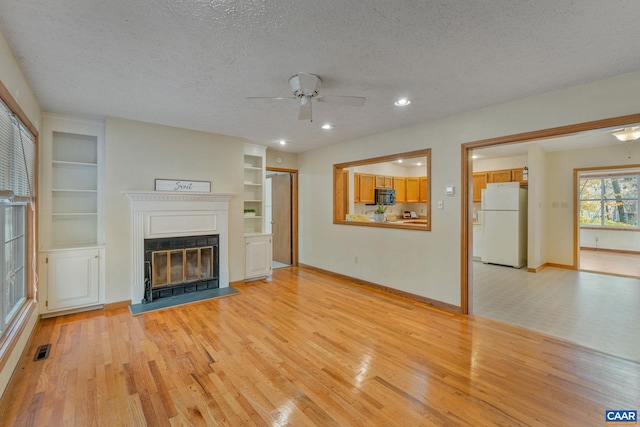 unfurnished living room with light hardwood / wood-style floors, built in features, a textured ceiling, and ceiling fan