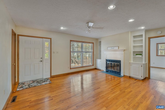 unfurnished living room with ceiling fan, light hardwood / wood-style floors, a textured ceiling, and a healthy amount of sunlight