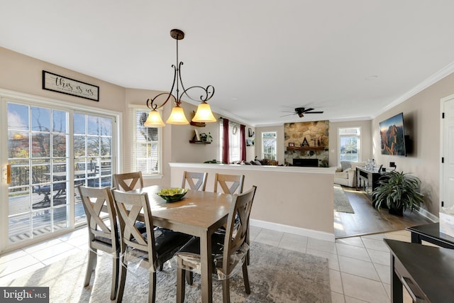 dining space with a stone fireplace, light hardwood / wood-style floors, ornamental molding, and ceiling fan with notable chandelier