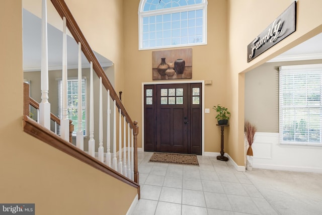 foyer entrance with crown molding, light colored carpet, and a high ceiling