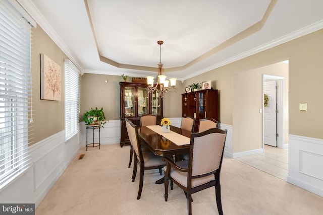 carpeted dining area with a notable chandelier, a raised ceiling, and ornamental molding