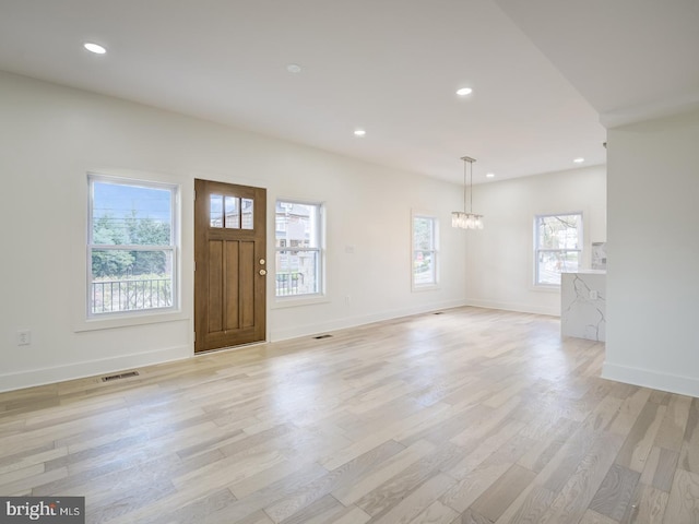 foyer with an inviting chandelier, plenty of natural light, and light hardwood / wood-style flooring