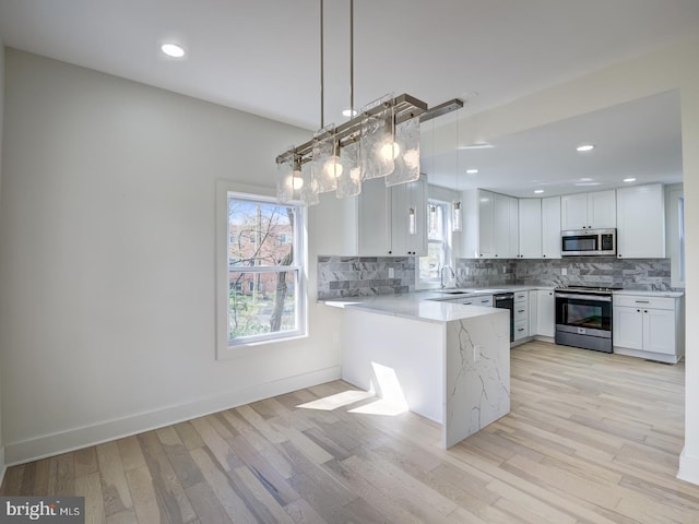 kitchen with stainless steel appliances, white cabinets, kitchen peninsula, light hardwood / wood-style flooring, and decorative light fixtures