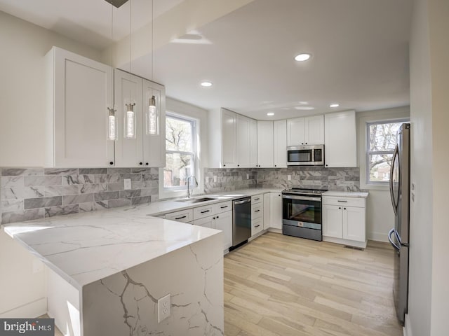 kitchen with white cabinetry, sink, appliances with stainless steel finishes, light stone countertops, and pendant lighting