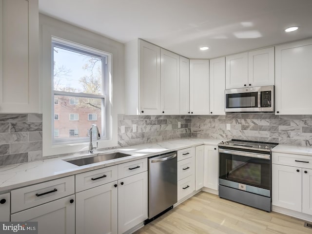 kitchen with white cabinets, light hardwood / wood-style flooring, sink, tasteful backsplash, and appliances with stainless steel finishes