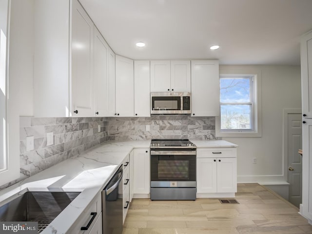 kitchen featuring white cabinetry, light wood-type flooring, stainless steel appliances, and light stone countertops