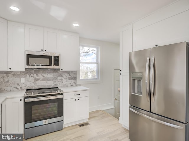 kitchen featuring stainless steel appliances, white cabinetry, backsplash, and light wood-type flooring