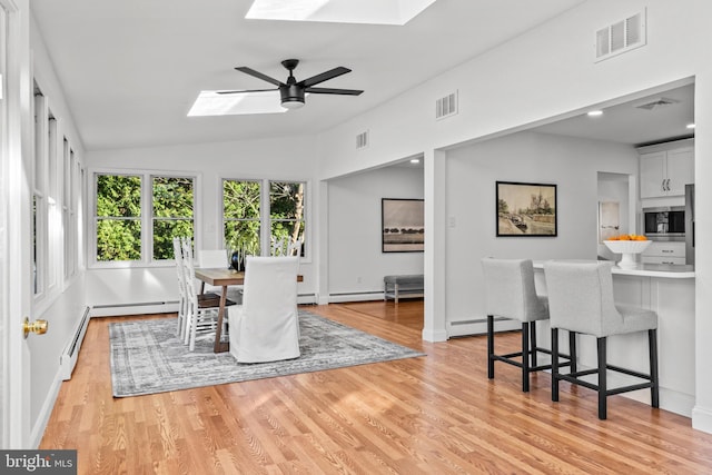 dining room featuring ceiling fan, a baseboard heating unit, light wood-type flooring, and lofted ceiling with skylight