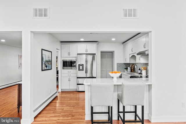 kitchen featuring a baseboard heating unit, a kitchen breakfast bar, stainless steel appliances, and white cabinets