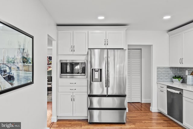 kitchen featuring stainless steel appliances, light hardwood / wood-style floors, white cabinetry, and decorative backsplash