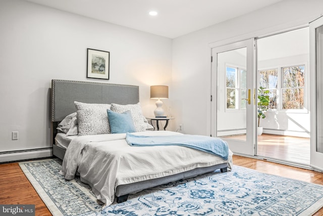 bedroom featuring access to exterior, a baseboard heating unit, and wood-type flooring