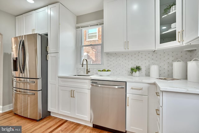 kitchen with sink, light stone countertops, appliances with stainless steel finishes, light hardwood / wood-style floors, and white cabinetry