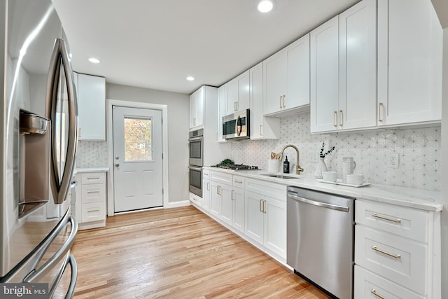 kitchen featuring decorative backsplash, stainless steel appliances, sink, light hardwood / wood-style flooring, and white cabinets