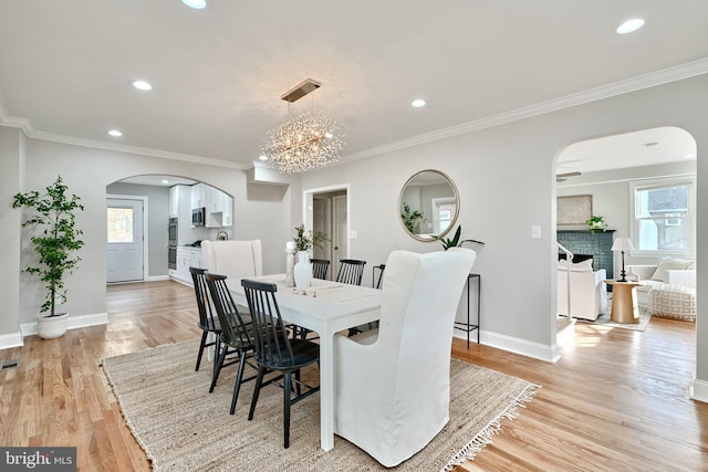 dining space featuring a notable chandelier, light wood-type flooring, crown molding, and a brick fireplace