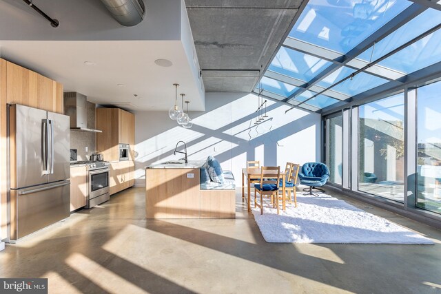 kitchen featuring sink, wall chimney exhaust hood, stainless steel appliances, a wall of windows, and decorative light fixtures