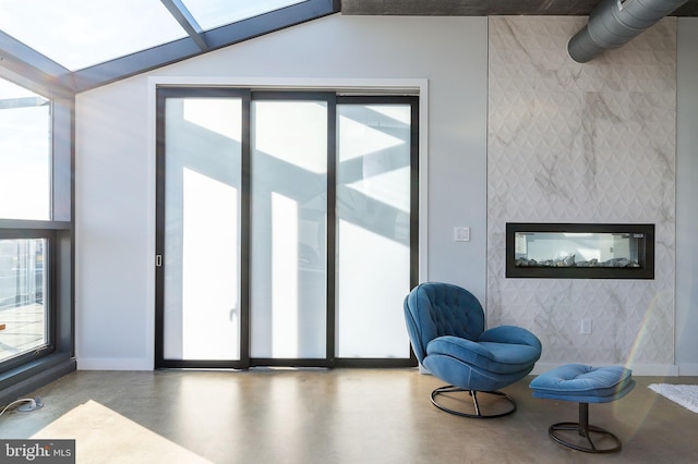 sitting room featuring a healthy amount of sunlight, concrete flooring, a tile fireplace, and vaulted ceiling