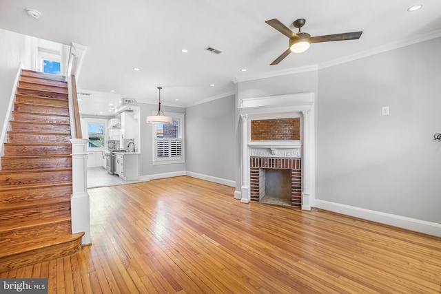 unfurnished living room with ceiling fan, a fireplace, light wood-type flooring, and crown molding