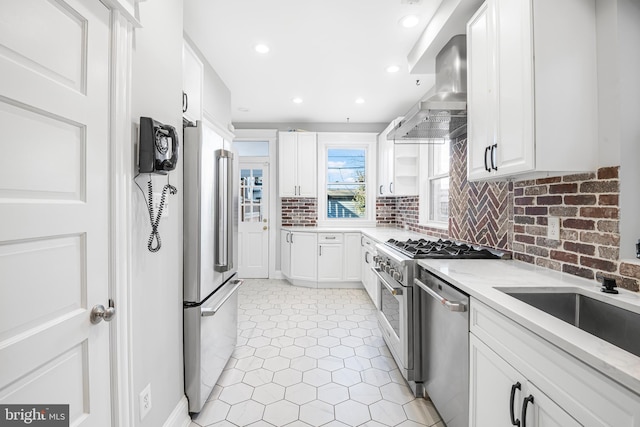 kitchen featuring white cabinetry, light stone countertops, wall chimney range hood, decorative backsplash, and appliances with stainless steel finishes