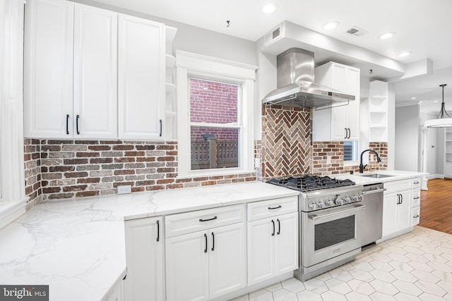 kitchen featuring white cabinetry, sink, hanging light fixtures, stainless steel appliances, and wall chimney range hood