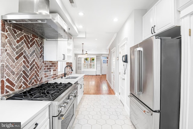 kitchen featuring high end appliances, white cabinets, wall chimney range hood, sink, and light wood-type flooring