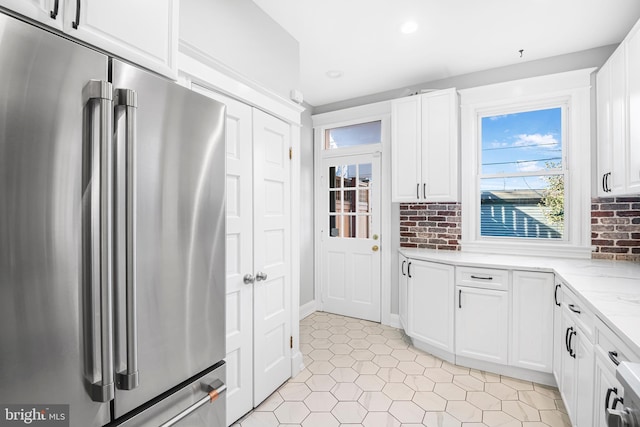 kitchen with backsplash, stainless steel refrigerator, white cabinetry, and light stone counters