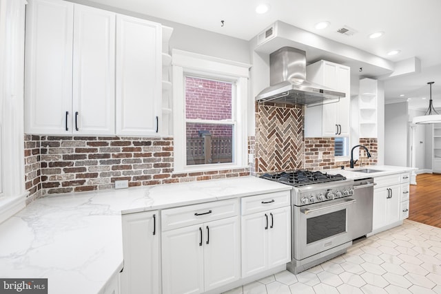 kitchen featuring stainless steel appliances, sink, wall chimney range hood, white cabinetry, and hanging light fixtures