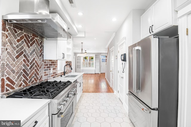 kitchen featuring white cabinetry, hanging light fixtures, wall chimney range hood, premium appliances, and light hardwood / wood-style flooring