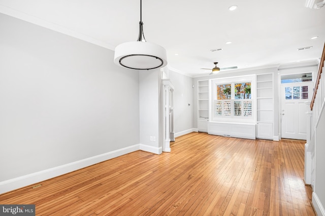 unfurnished dining area with ceiling fan, built in features, ornamental molding, and light hardwood / wood-style flooring