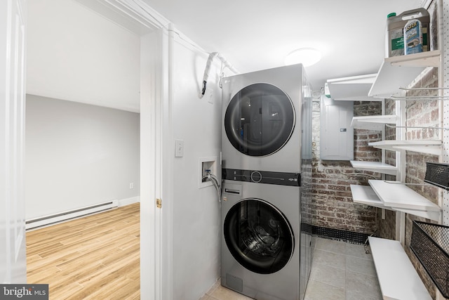 washroom with light hardwood / wood-style floors, baseboard heating, stacked washer / dryer, and brick wall