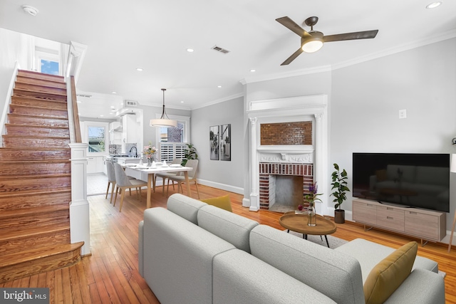 living room featuring a fireplace, light wood-type flooring, ceiling fan, and ornamental molding